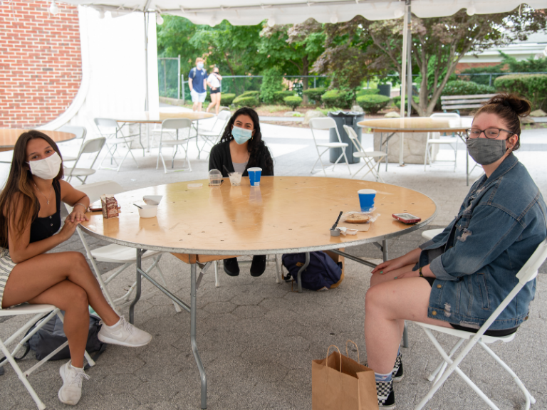 three female students sitting at table together under white tent outside